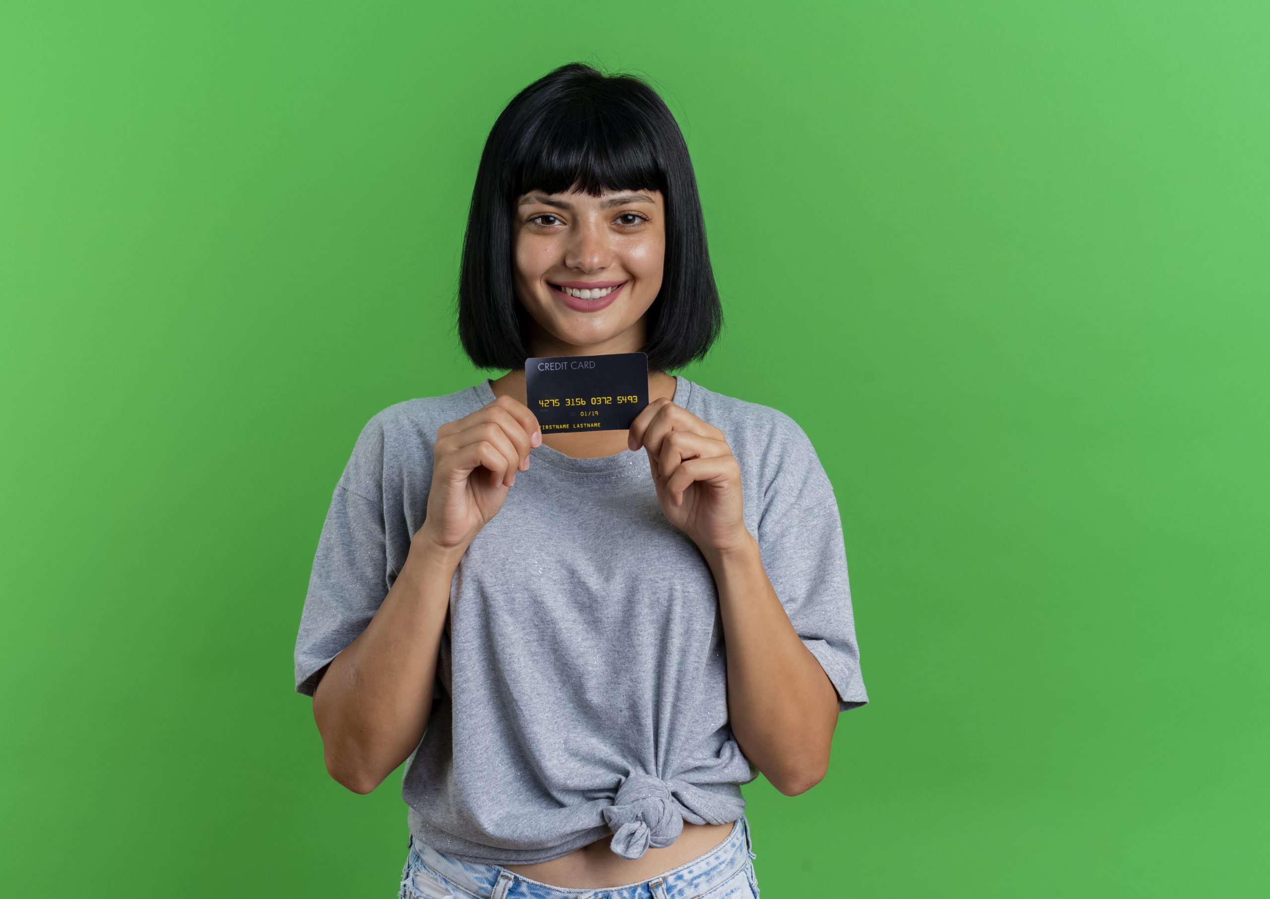 Smiling Young Brunette Caucasian Girl Holds Credit Card Looking Camera Isolated Green Background With Copy Space Scaled