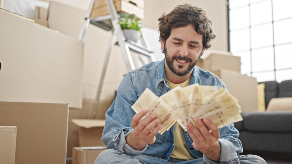 Young Hispanic Man Counting Denmark Krone Banknotes Sitting Floor New Home Scaled