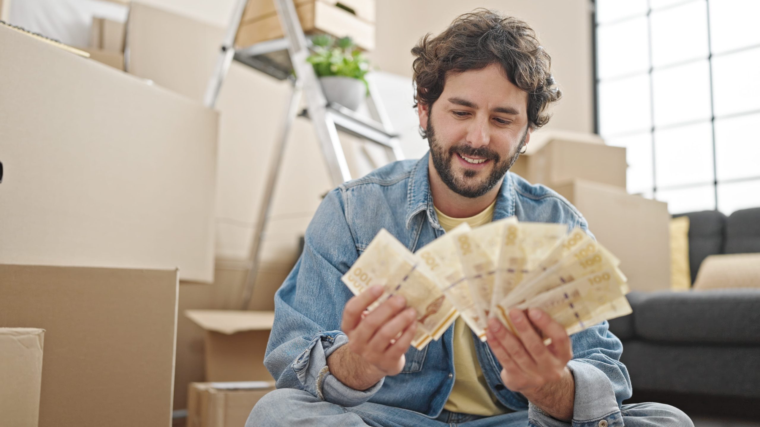 Young Hispanic Man Counting Denmark Krone Banknotes Sitting Floor New Home Scaled